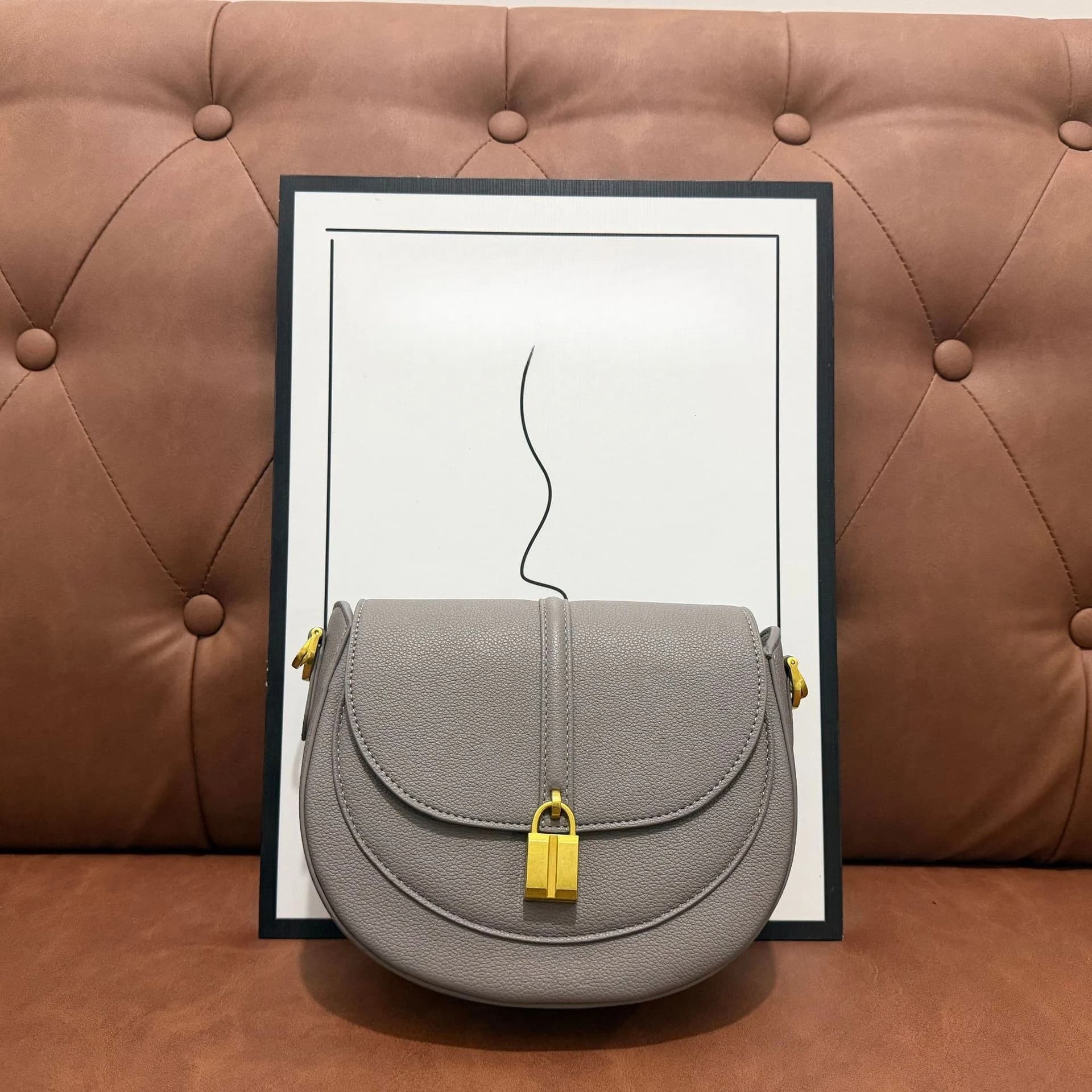 Bolsa transversal meia-lua em couro granulado, com fecho de cadeado metálico e alça ajustável para uso diário.
